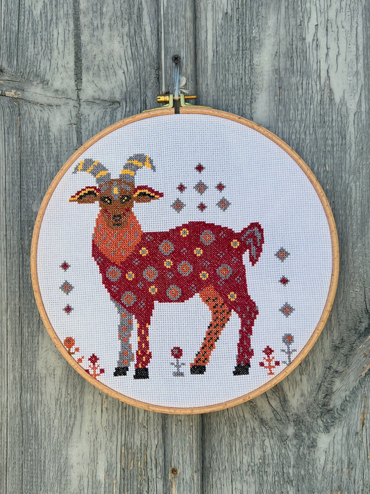 Cross-stitched goat design in an embroidery hoop on a wooden surface