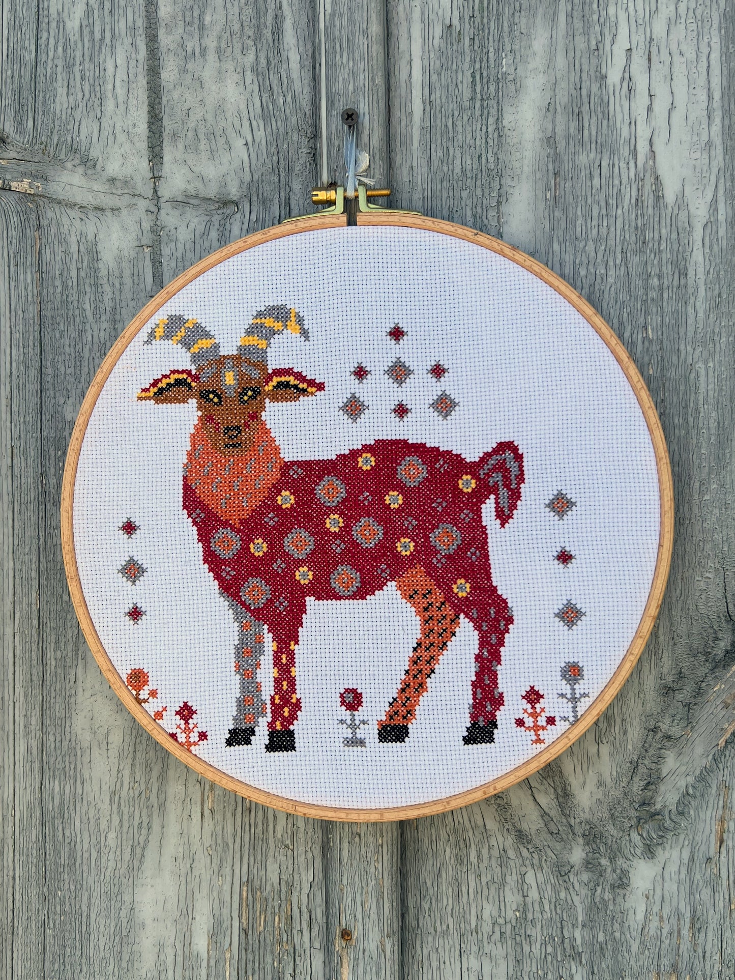 Cross-stitched goat design in an embroidery hoop on a wooden surface